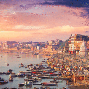 Sunrise view of Varanasi ghats on the banks of the Ganga River with colorful boats, crowded temples, historic buildings, and devotees gathered along the riverside.